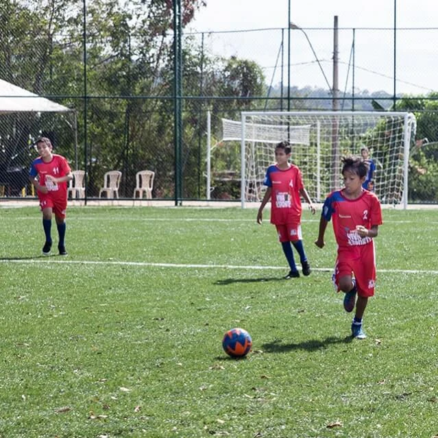 Crianças jogando bola num campo de futebol com uniforme do Instituto Ramacrisna